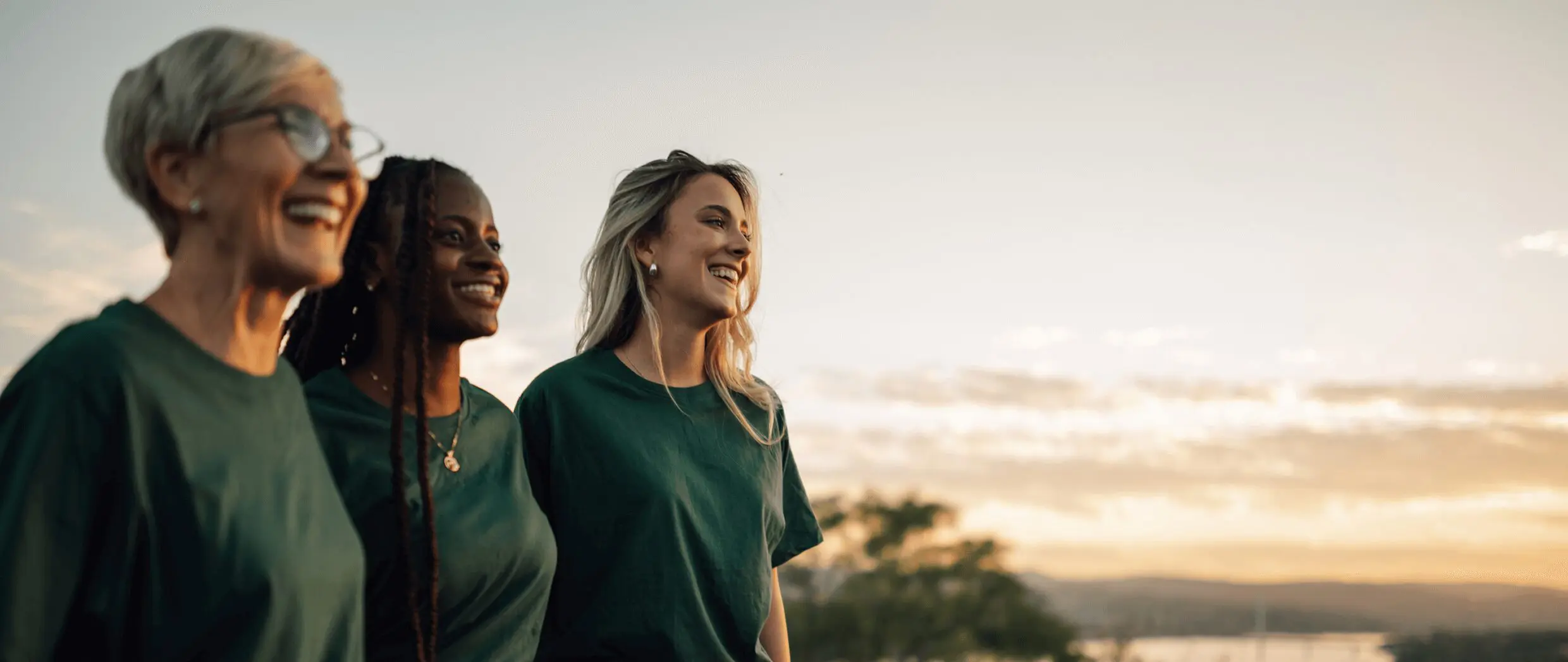 Three women smiling outdoors at sunset.